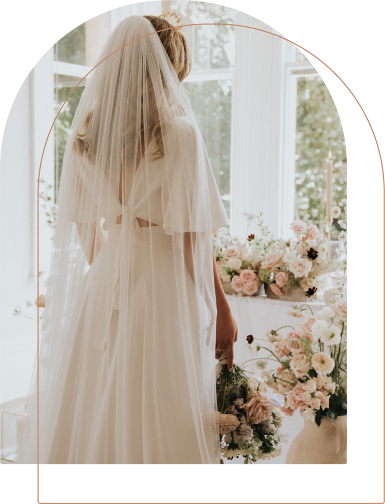 Bride in her wedding dress and veil surrounded by a stunning creation of flowers making an elegant wedding venue by wedding and events florist, Winter and the Willows